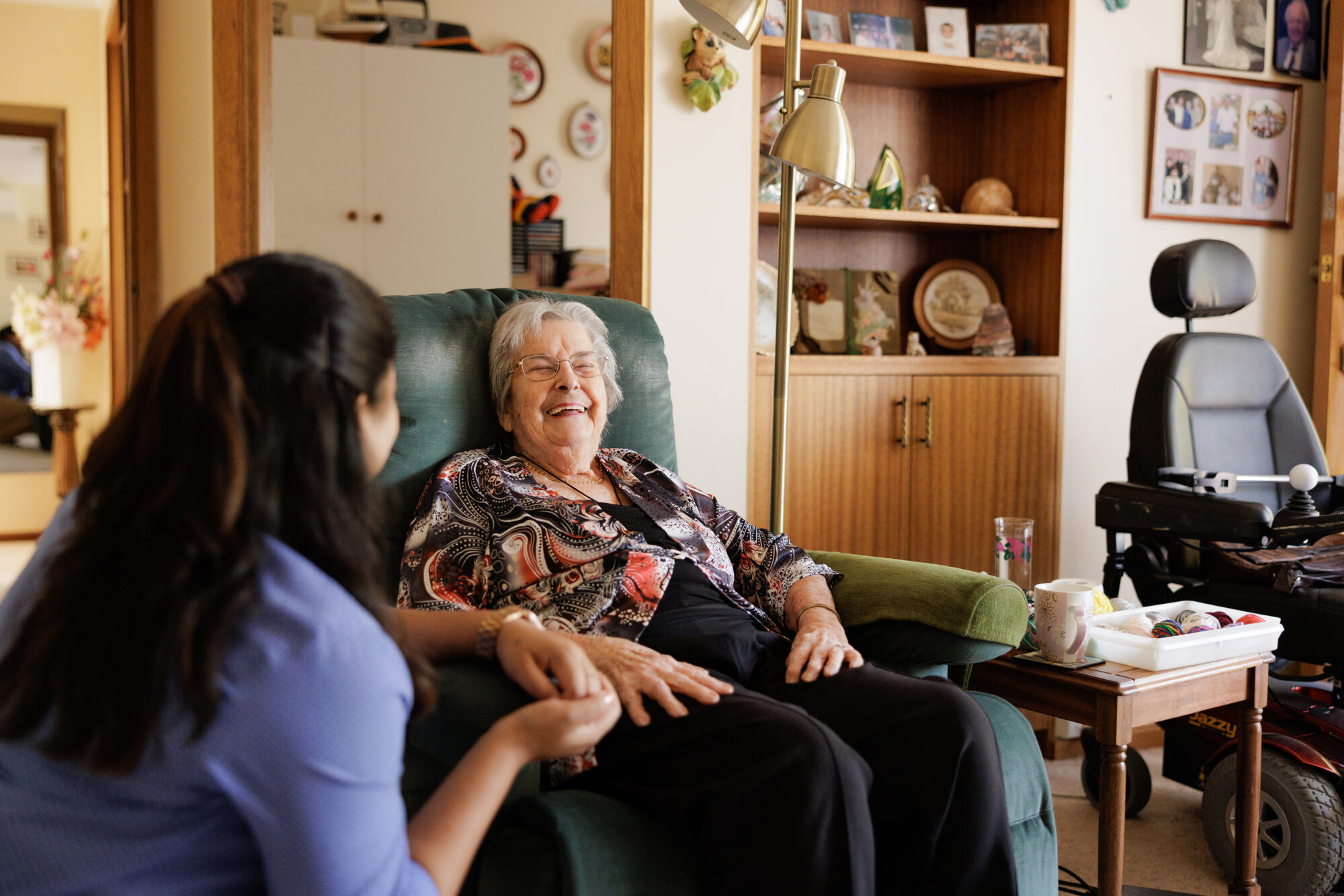 A carer sharing a warm laugh with a resident in her own room.