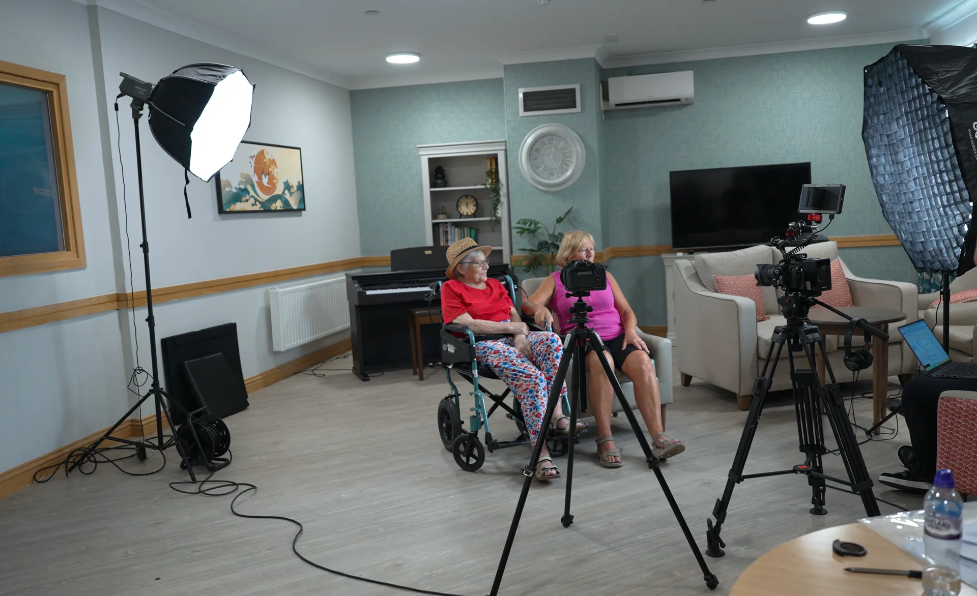 A small film crew quietly filming a carer and resident in a lounge.