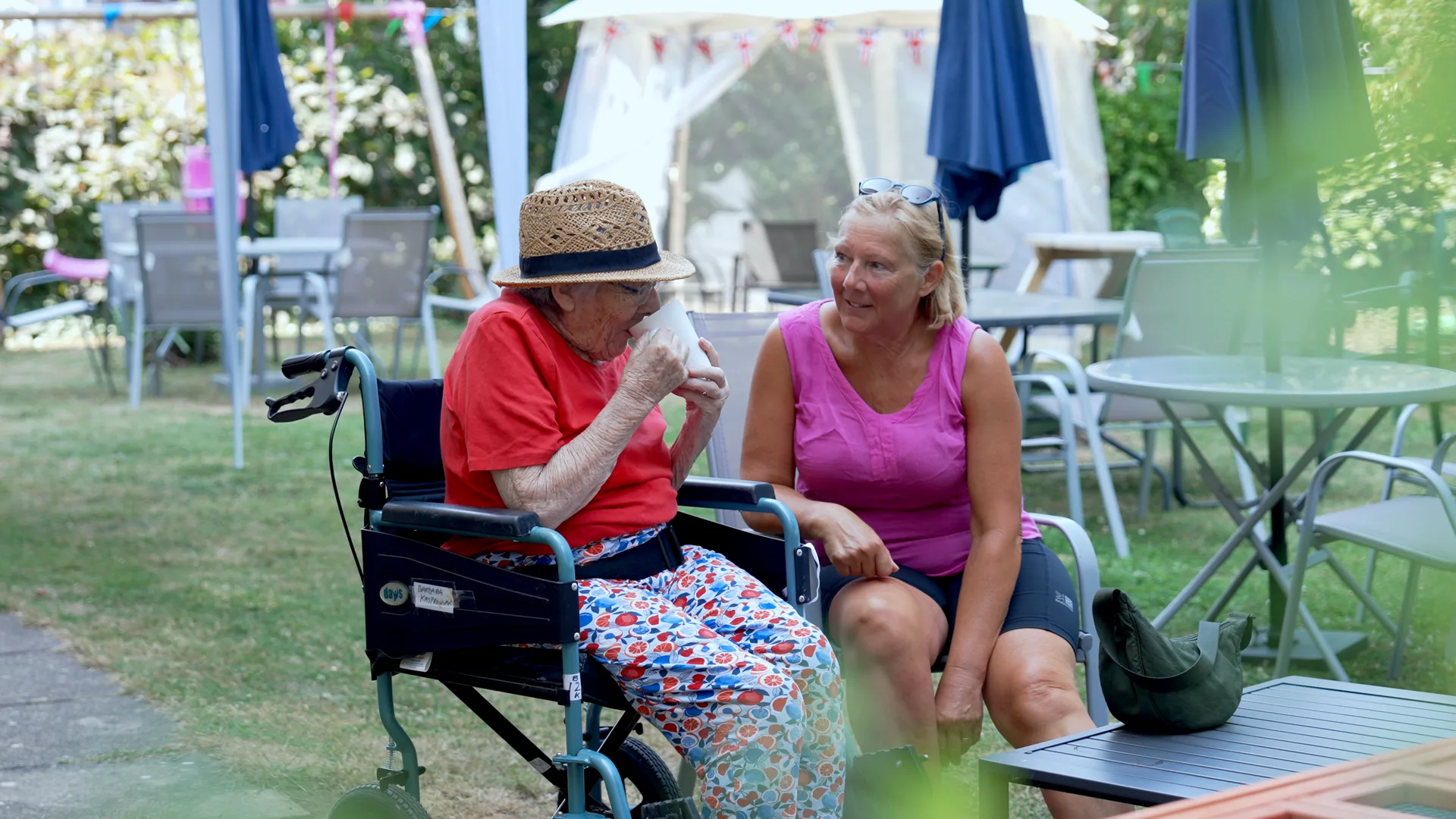A resident and a visiting family member enjoying a summer garden party at a care home.